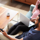 Couple Sitting On Sofa At Home Using Laptop Computer And Watching TV